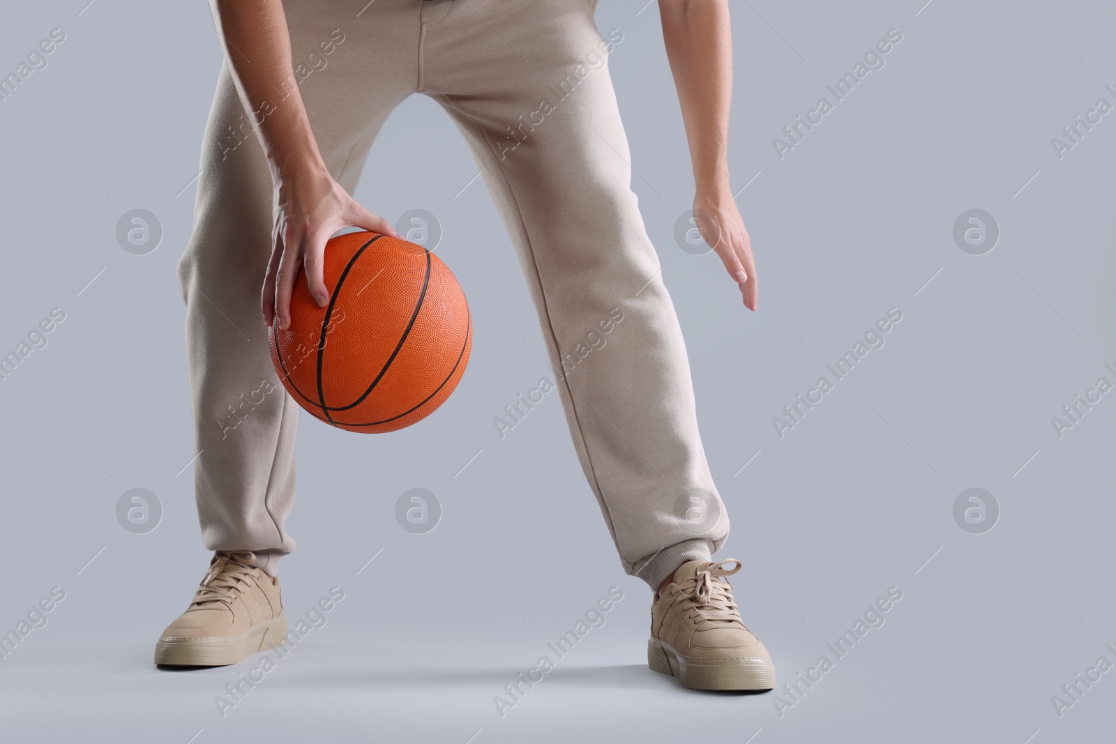 Photo of Man in stylish sneakers playing with basketball ball on light grey background, closeup