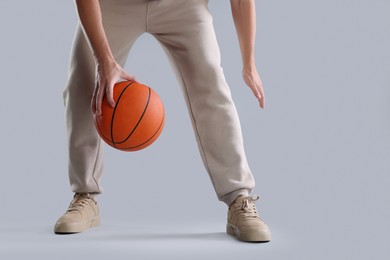 Photo of Man in stylish sneakers playing with basketball ball on light grey background, closeup