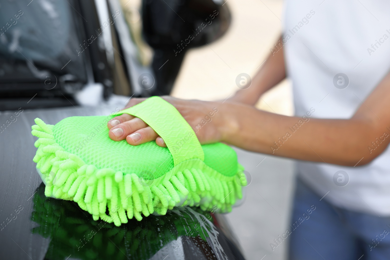 Photo of Woman washing car with sponge outdoors, closeup