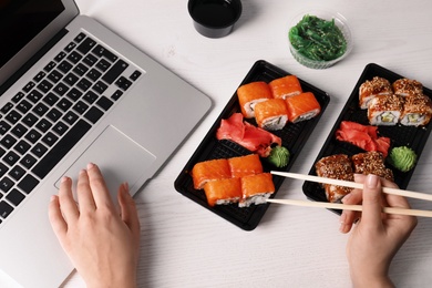 Photo of Woman eating tasty sushi rolls at workplace, closeup. Food delivery