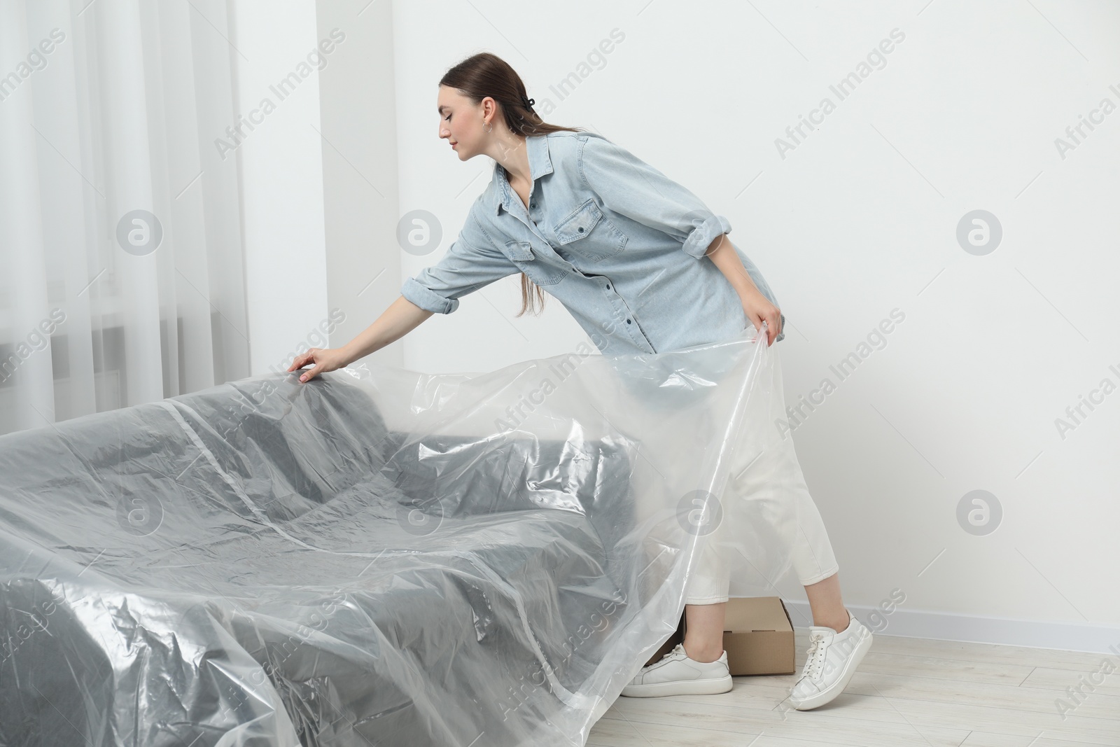 Photo of Young woman putting plastic film away from sofa at home