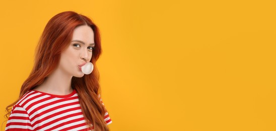 Photo of Portraitbeautiful woman blowing bubble gum on orange background. Space for text