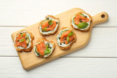 Photo of Tasty canapes with salmon, capers, cucumber and sauce on white wooden table, top view