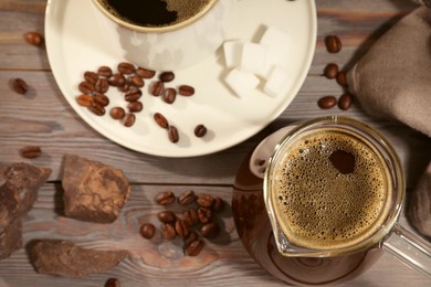 Glass turkish coffee pot with hot drink, chocolate and beans on wooden table, flat lay