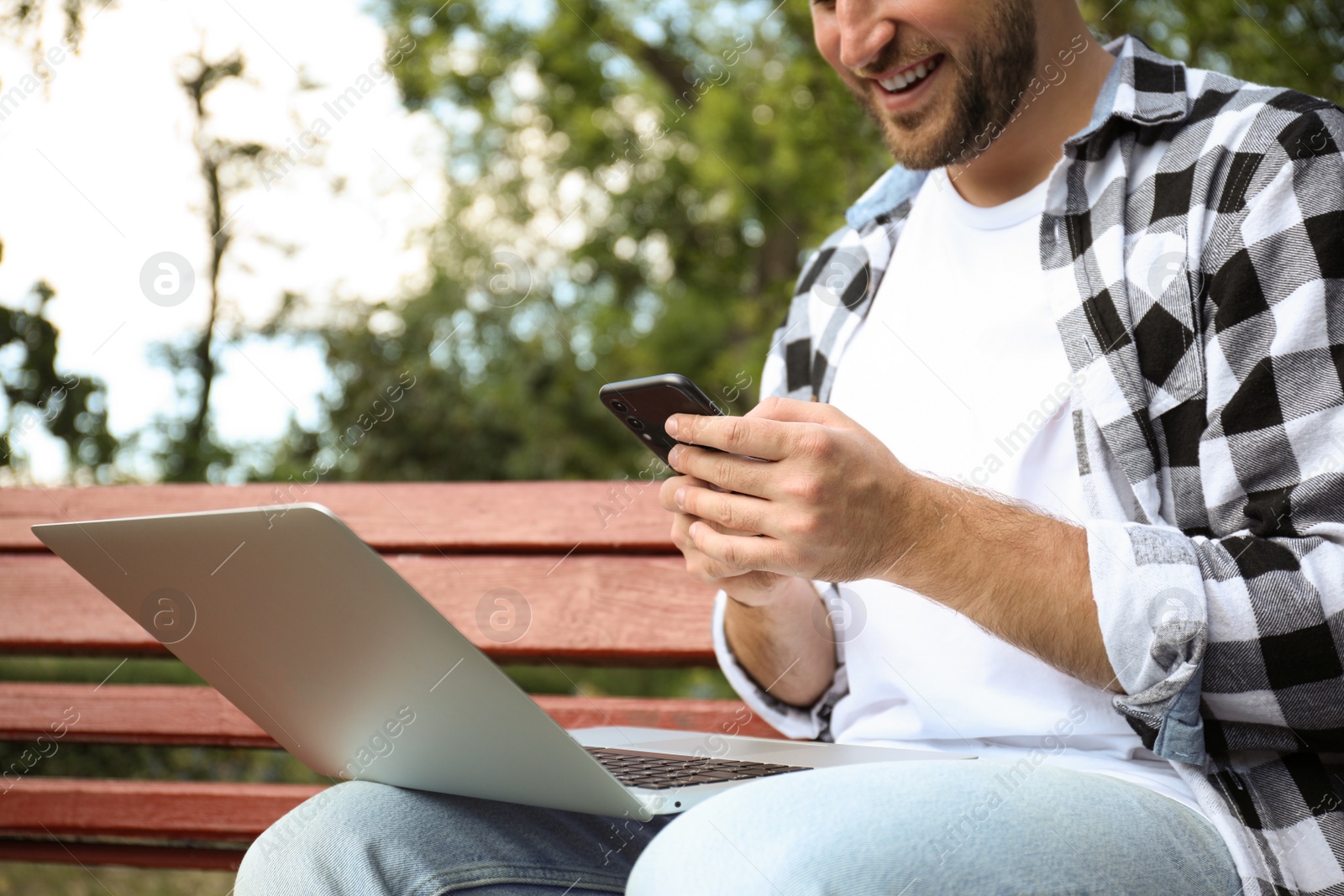 Photo of Young man with smartphone and laptop in park, closeup