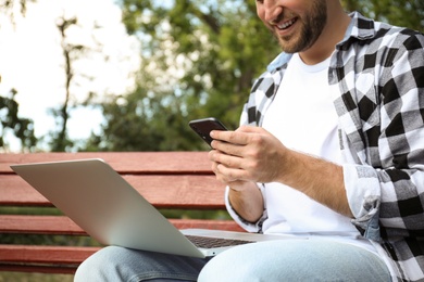 Young man with smartphone and laptop in park, closeup