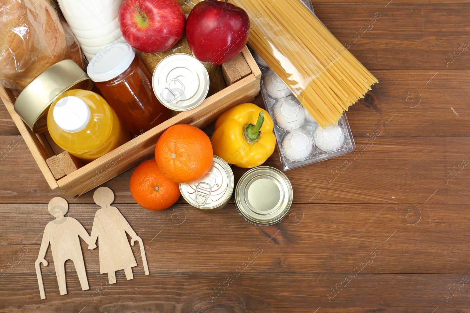 Photo of Humanitarian aid for elderly people. Different donation food products and figures of senior couple on wooden table, top view. Space for text