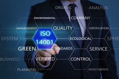 Businessman pointing at virtual icon with text ISO 14001 on color background, closeup 