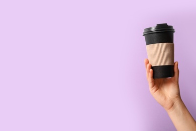 Photo of Woman holding takeaway paper coffee cup with cardboard sleeve on violet background, closeup. Space for text