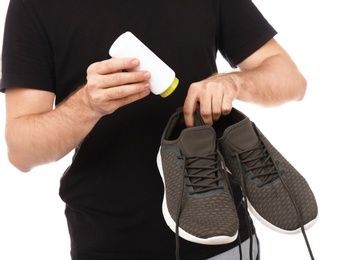 Young man putting powder freshener into shoes on white background