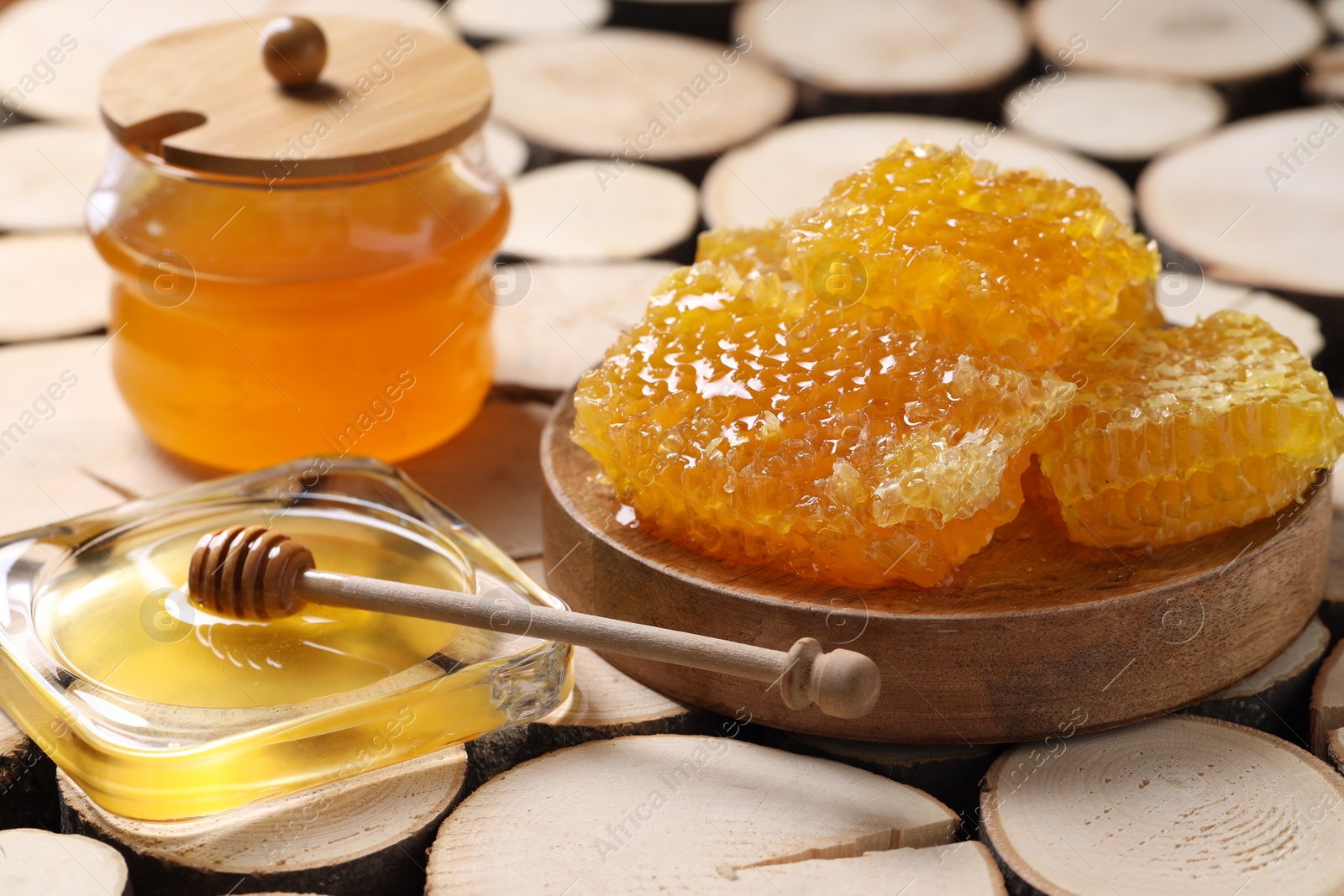 Photo of Natural honeycombs with honey and wooden dipper on textured table, closeup
