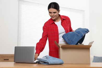 Young with just unpacked new jeans using laptop at table indoors. Online shopping