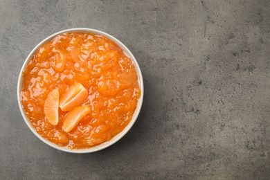 Photo of Tasty tangerine jam in bowl on grey table, top view. Space for text