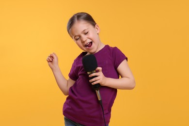 Photo of Cute little girl with microphone singing on yellow background