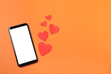Long-distance relationship concept. Smartphone and paper hearts on orange background, flat lay with space for text