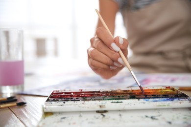 Photo of Young woman drawing with watercolors at table indoors, closeup. Space for text