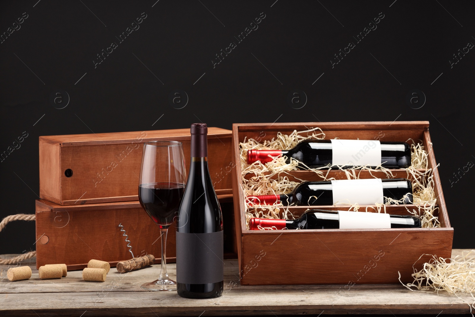 Photo of Box with wine bottles, glass, corks and corkscrew on wooden table against black background