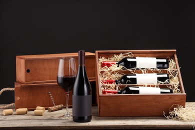 Photo of Box with wine bottles, glass, corks and corkscrew on wooden table against black background