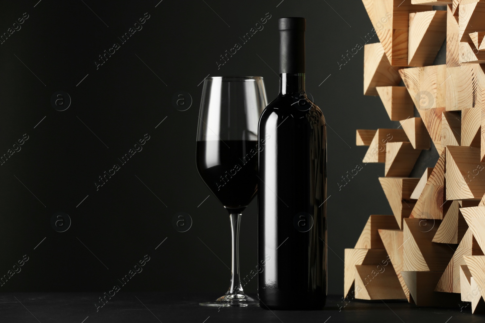 Photo of Stylish presentation of red wine in bottle and wineglass on black background, space for text