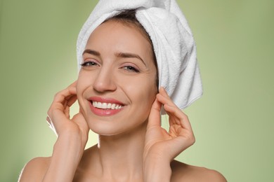 Photo of Beautiful young woman with hair wrapped in towel after washing on light green background