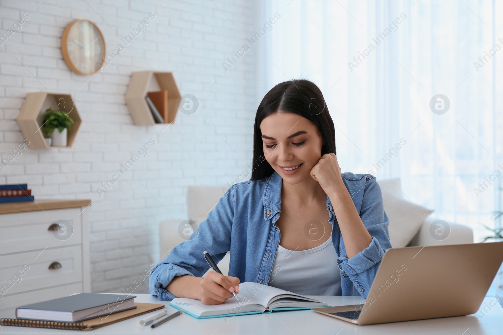 Photo of Young woman taking notes during online webinar at table indoors