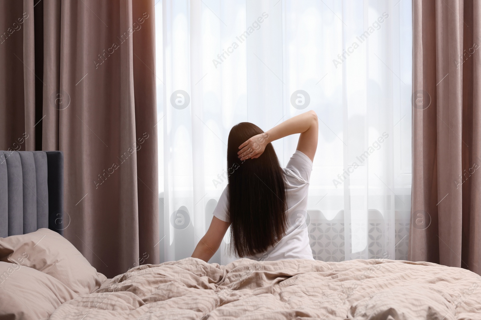 Photo of Woman stretching on bed at home, back view. Lazy morning