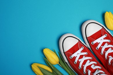 Photo of Pair of new stylish red sneakers and beautiful tulips on light blue background, flat lay. Space for text