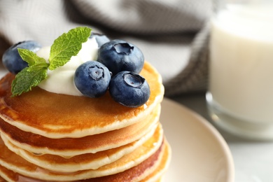 Photo of Plate of tasty pancakes with blueberries, sauce and mint on table, closeup