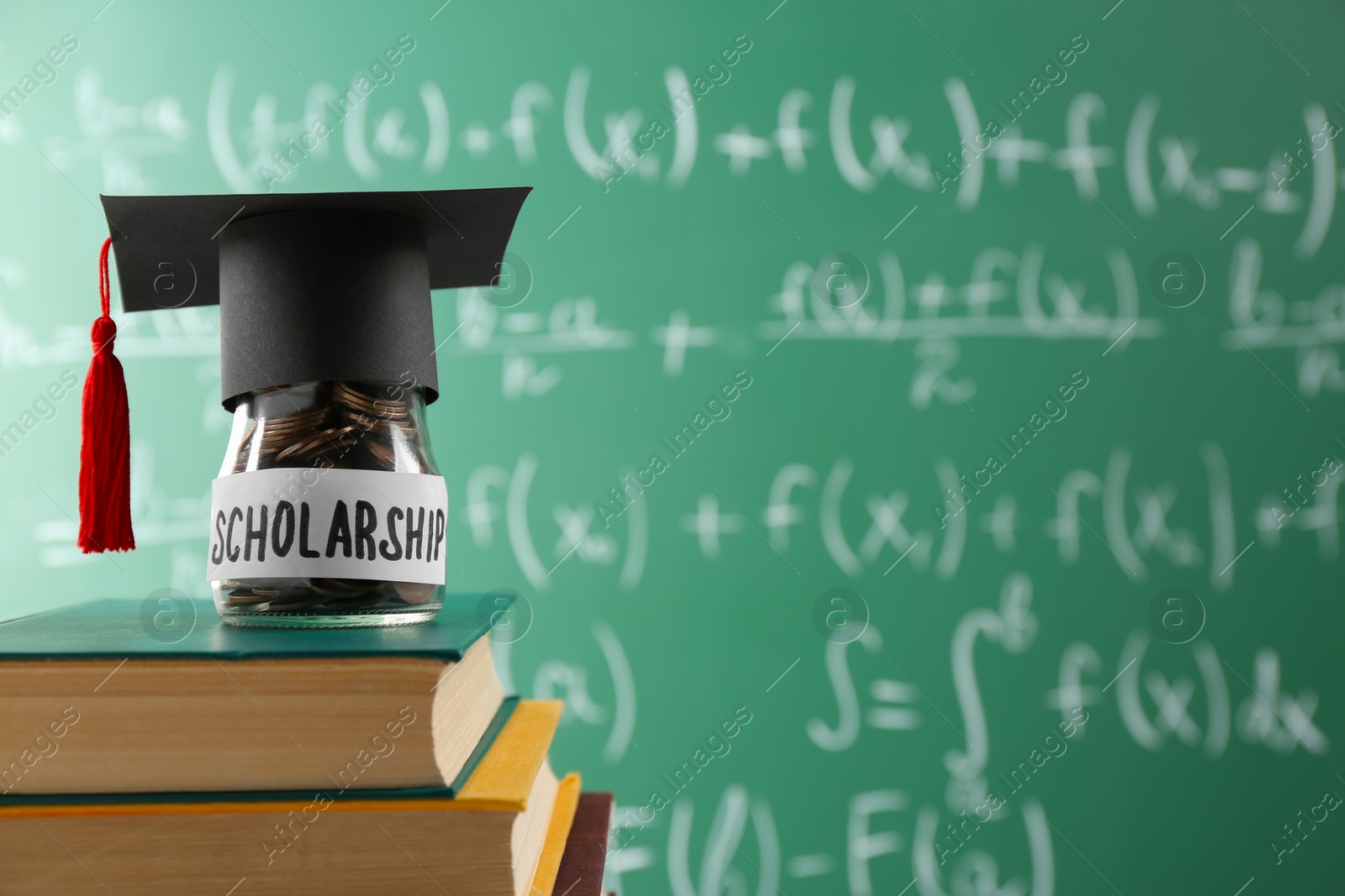 Photo of Scholarship concept. Glass jar with coins, graduation cap and books against greenboard, space for text