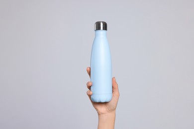 Photo of Woman holding thermo bottle on light grey background, closeup