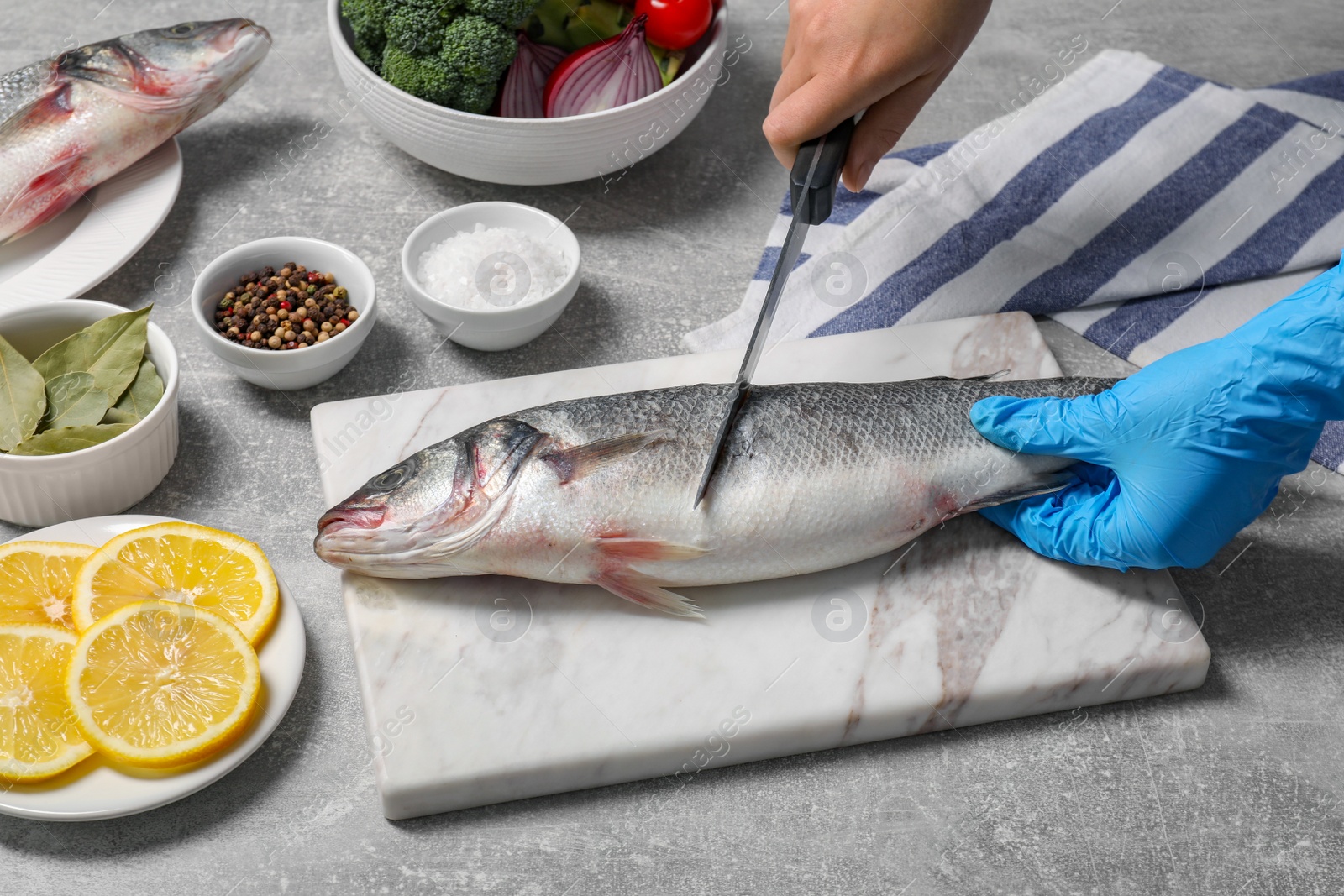 Photo of Woman cutting fresh raw sea bass fish at light gray table, closeup