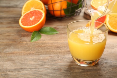 Photo of Pouring delicious orange juice into glass on wooden table, closeup. Space for text