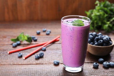 Photo of Glass of blueberry smoothie with mint on wooden table, space for text