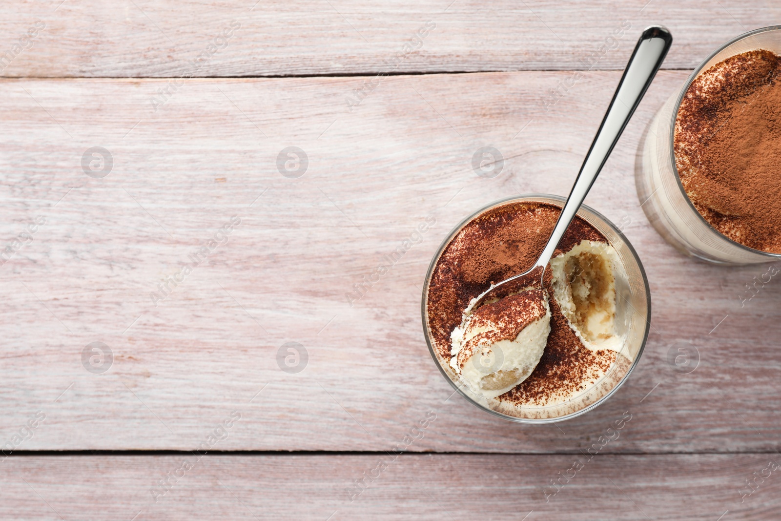 Photo of Delicious tiramisu in glasses and spoon on wooden table, top view. Space for text