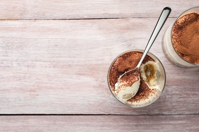 Delicious tiramisu in glasses and spoon on wooden table, top view. Space for text