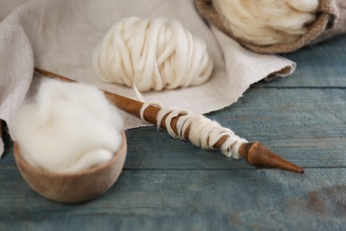 Photo of Soft white wool and spindle on blue wooden table