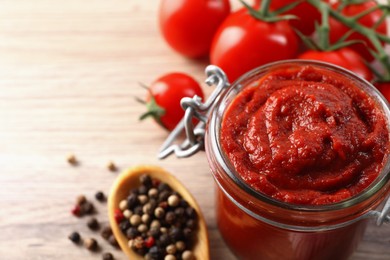 Photo of Jar of tasty tomato paste and ingredients on wooden table, closeup. Space for text