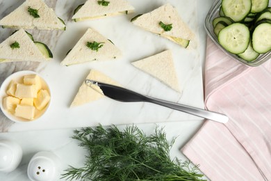 Spreading butter on tasty sandwiches with cucumber and parsley on white marble table, flat lay