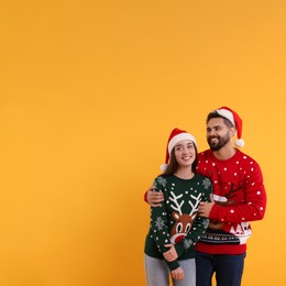 Happy young couple in Christmas sweaters and Santa hats on orange background. Space for text