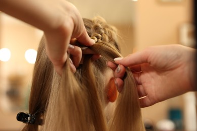 Photo of Professional hairdresser braiding girl's hair in beauty salon, closeup