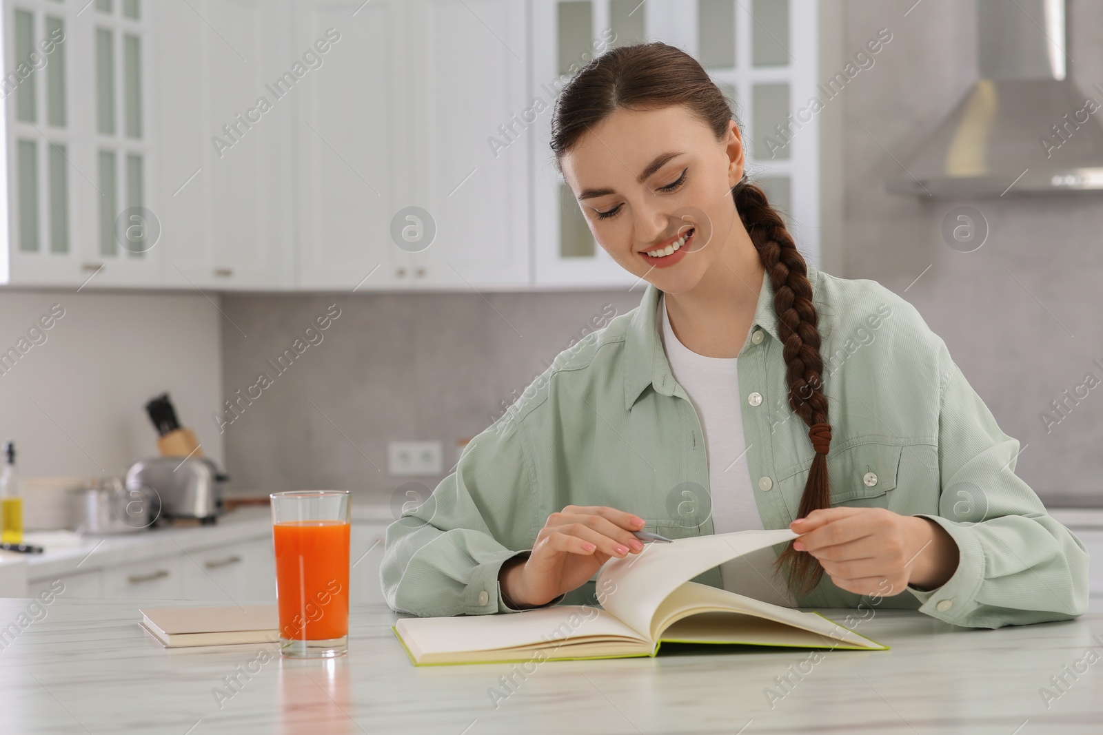 Photo of Beautiful young woman with notebook at white marble table in kitchen