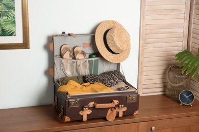 Vintage suitcase with clothes and shoes on chest of drawers indoors