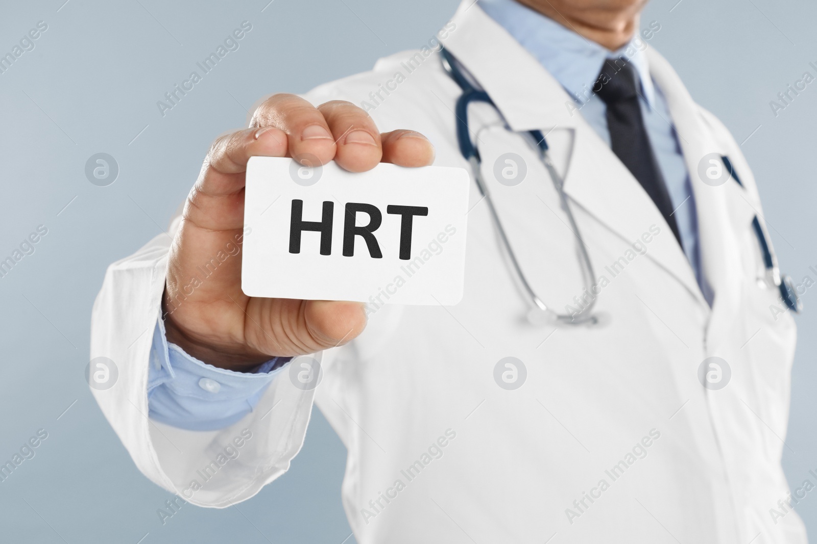 Image of Doctor holding card with abbreviation HRT on light grey background, closeup. Hormone Replacement Therapy