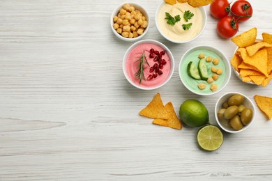 Photo of Different kinds of tasty hummus served with nachos on white wooden table, flat lay. Space for text
