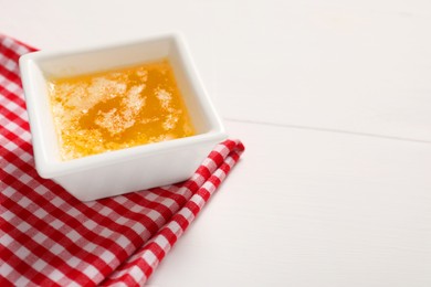 Photo of Melted butter in bowl on white wooden table, closeup. Space for text