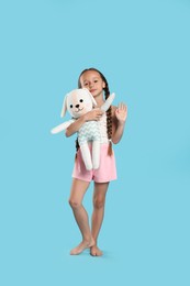 Photo of Cute girl wearing pajamas with toy on light blue background