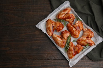 Photo of Raw marinated chicken wings and rosemary on wooden table, top view. Space for text