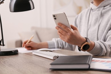 Photo of Young woman with smart watch and phone at table in office, closeup