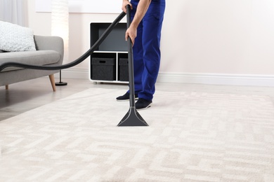 Photo of Man removing dirt from carpet with vacuum cleaner indoors, closeup