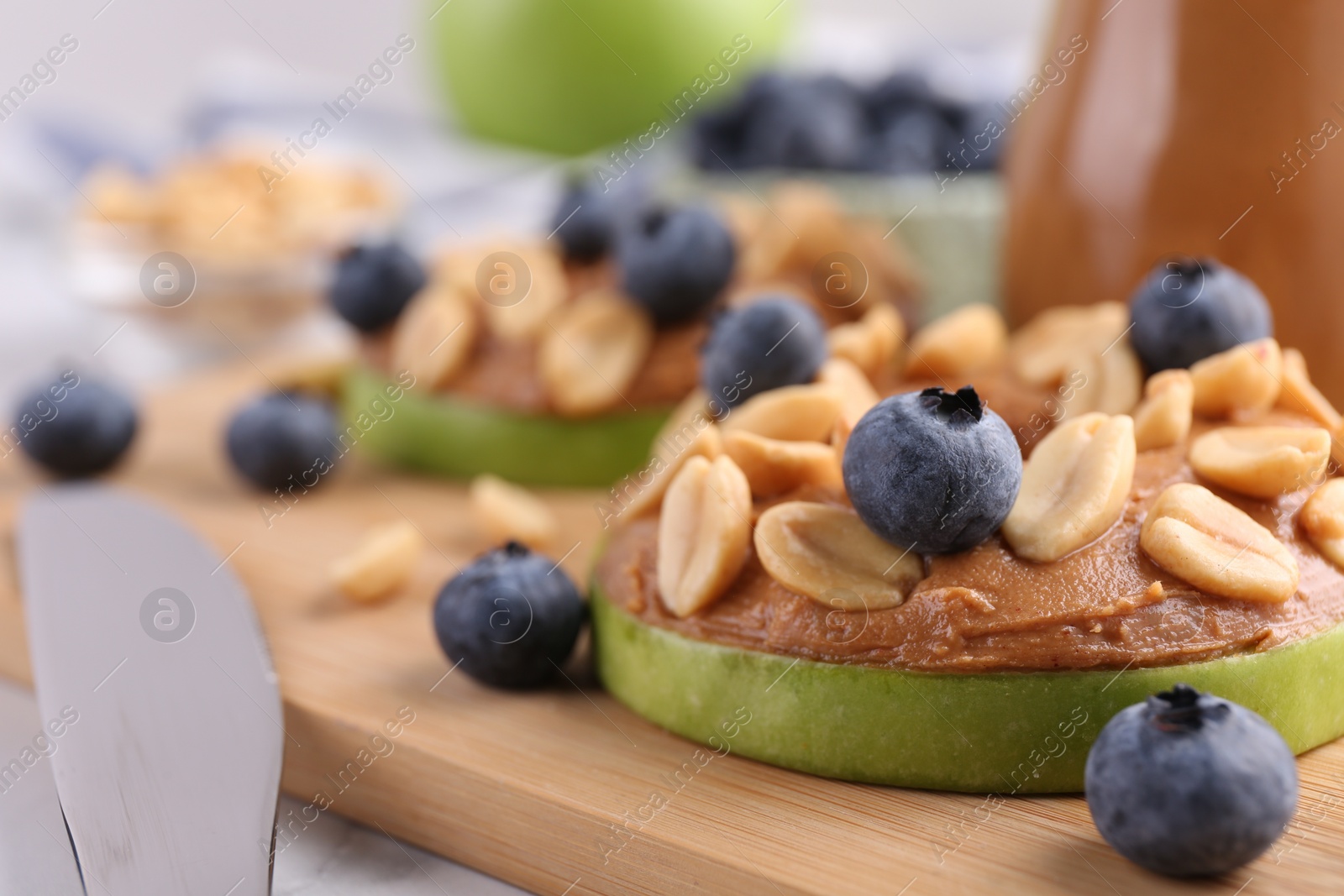 Photo of Slice of fresh apple with peanut butter, blueberries and nuts on table, closeup